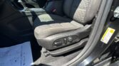 Front interior of a car showing the driver seat and center console, with a red seat belt buckle and textured seat fabric in dark tones.