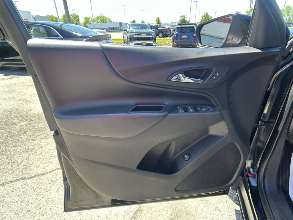 Interior of a car door panel with a chrome handle, window controls, and side mirror visible through the open door