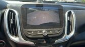 Infotainment screen showing a car’s rear‑view camera, with parking guidelines over a busy lot and cars in the distance.