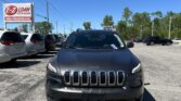 Front view of a dark gray Jeep SUV parked in a car dealership lot, with an E-Z LOAN Auto Sales sign on the left and a blue sky above.