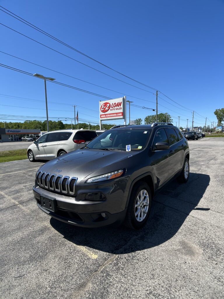 Foregrounded gray Jeep SUV in a dealership lot with an EZ LOAN AUTO SALES sign in the background against a clear blue sky