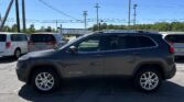Gray Jeep Cherokee parked in a lot with other vehicles and utility poles overhead under a clear blue sky.