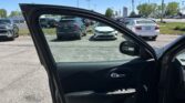 Open car door in the foreground to a busy parking lot with multiple parked cars under a bright blue sky.