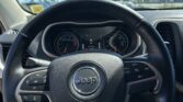 Driver’s-eye view of a Jeep steering wheel with the dashboard gauges in the background and a bright blue sky through the windshield, in a parking lot