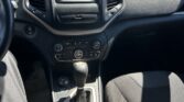 Car interior: center touchscreen with radio/climate controls and gear shifter; dealership lot seen through windshield