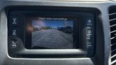 Dashboard touchscreen showing a rearview camera feed with the message 'Check entire surroundings' while parked in a lot.