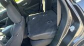 Open car door reveals the backs of the rear seats folded down with visible seatbelts and the front seat nearby, showing the interior cargo area of a dark car