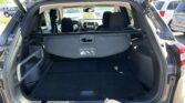 Open tailgate of a dark SUV showing the cargo area with rear seats visible and a sunroof canopy overhead in a parking lot.