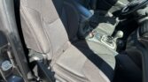 Interior of a car showing black fabric front seats with contrast stitching and center console; driver's side door and steering wheel visible in daytime light.