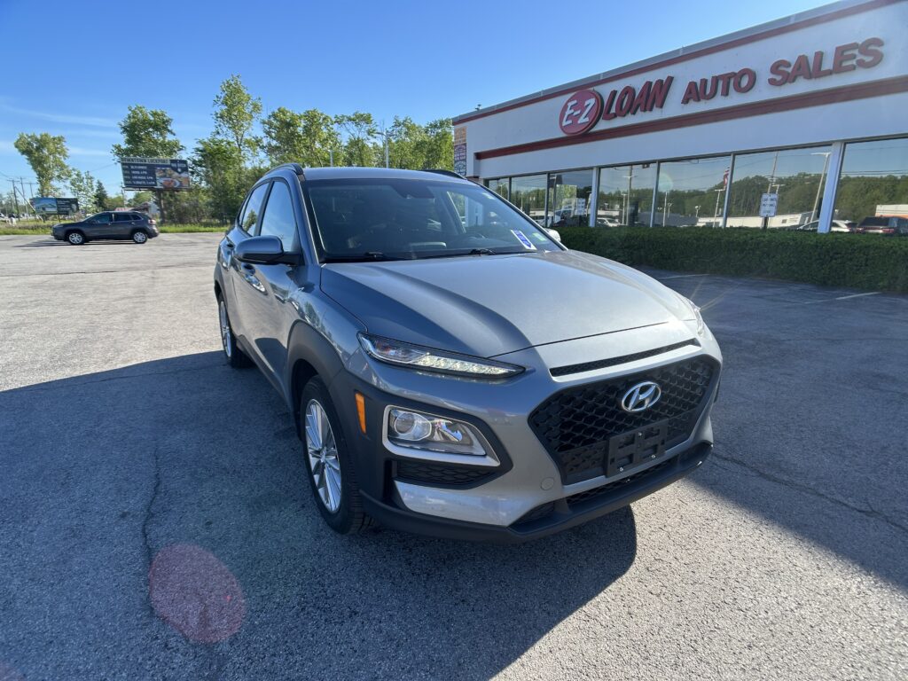 Silver Hyundai SUV in a parking lot in front of the EZ Auto Sales building with a clear blue sky above.