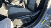 Front interior of a car: center console with gear shifter, handbrake, and patterned cloth seats; paper on the floor near the door.