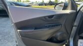 Open car door view showing the inner door panel with window controls and speaker; a car dealership lot is visible outside the window.