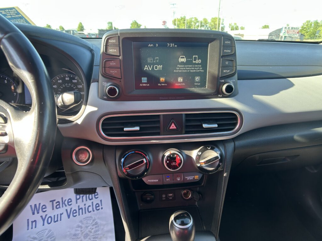 Center-console view of a car interior with the touchscreen showing 'AV Off', surrounding physical buttons, and steering wheel to the left.