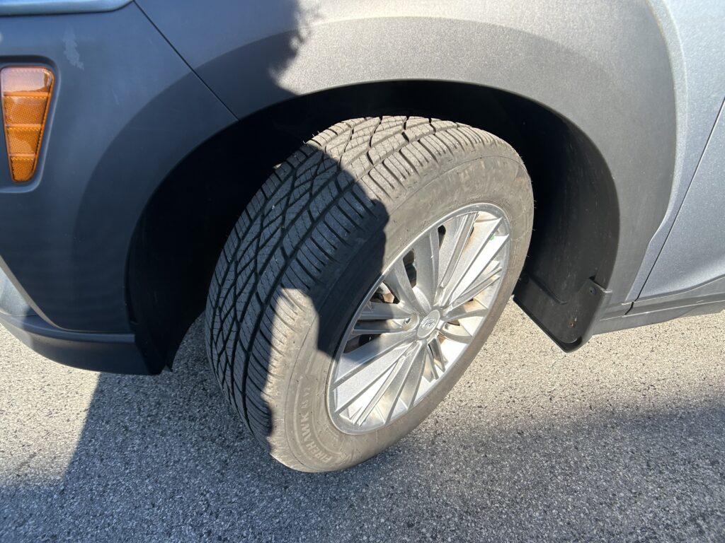 Close-up of a car's front wheel and fender, showing the tire tread and an orange turn signal on a blue vehicle.