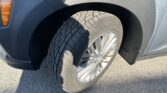 Close-up of a car's front wheel and fender, showing the tire tread and an orange turn signal on a blue vehicle.