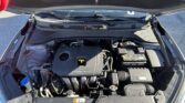 Front of a car with the hood open, showing the engine bay, battery, and various hoses and components.