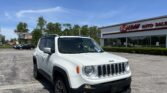 White Jeep Renegade parked in front of E-Z Loan Auto Sales on a sunny day in the dealership lot outside the showroom.
