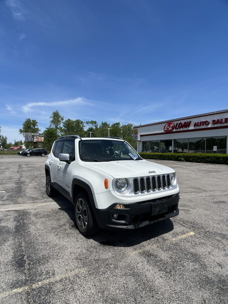 White Jeep Renegade parked in front of E-Z Loan Auto Sales on a sunny day in the dealership lot outside the showroom.