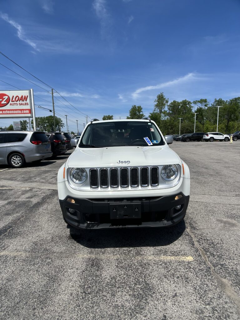 Front view of a white Jeep SUV in a car dealership lot, with a blue sky and EZ LOAN Auto Sales sign nearby.