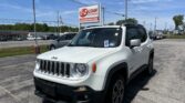 White Jeep SUV in a dealership lot with an EZ Loan Auto Sales sign and an American flag under a clear blue sky.