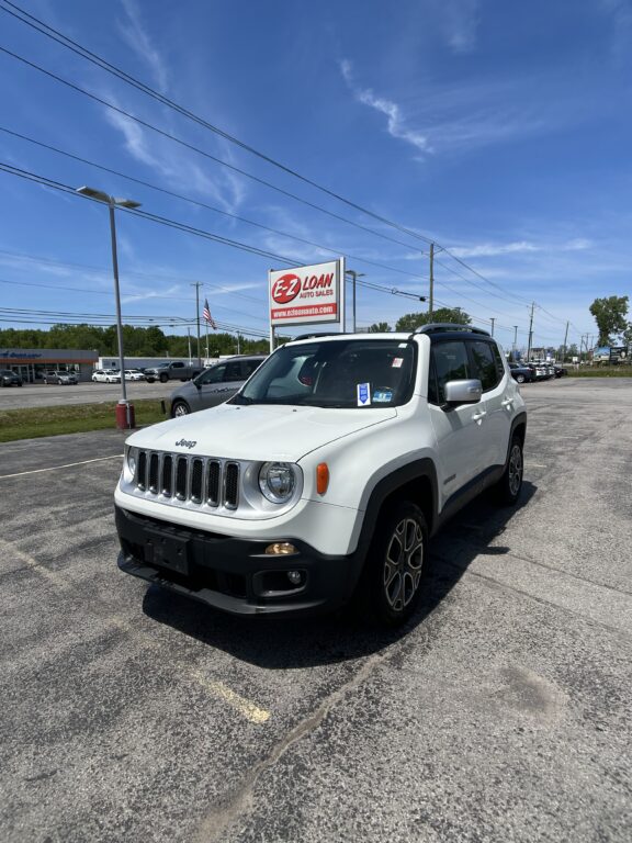 White Jeep SUV in a dealership lot with an EZ Loan Auto Sales sign and an American flag under a clear blue sky.