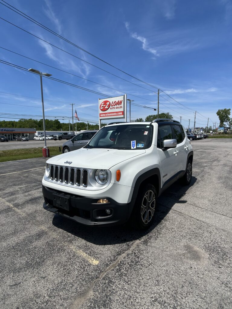 White Jeep SUV in a dealership lot with an EZ Loan Auto Sales sign and an American flag under a clear blue sky.