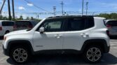 White Jeep Renegade parked in a lot with other vehicles; blue sky and power lines overhead, foreground car visible in side view.