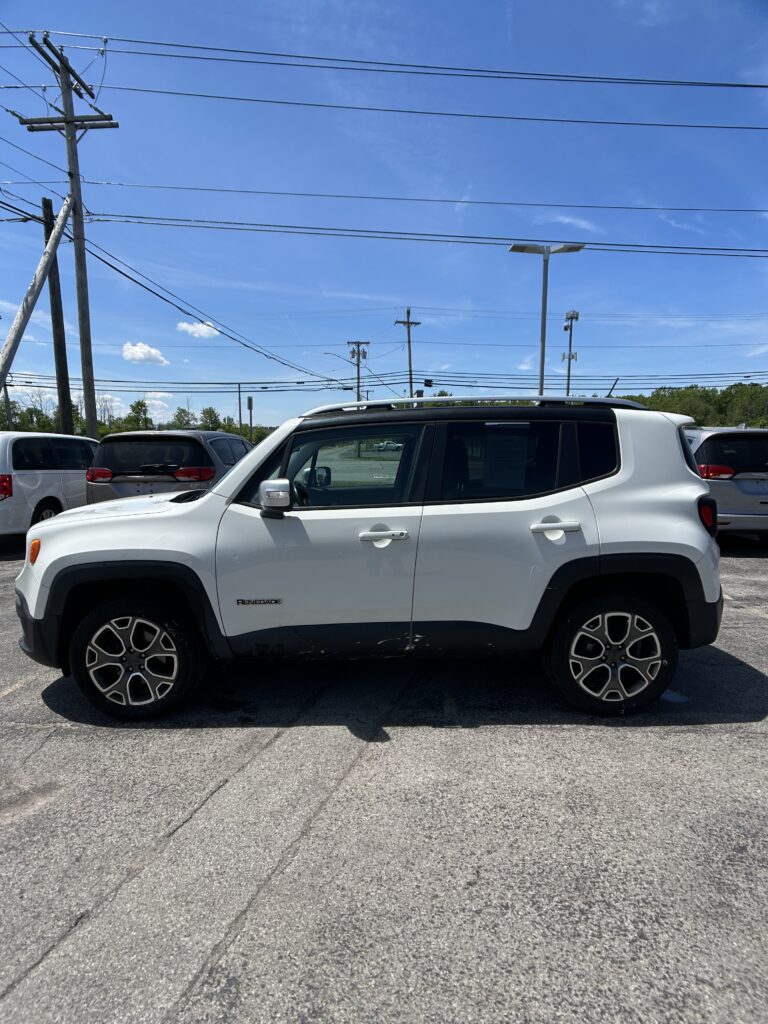 White Jeep Renegade parked in a lot with other vehicles; blue sky and power lines overhead, foreground car visible in side view.