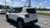 White Jeep SUV parked in a lot with power lines overhead and a bright blue sky in the background.