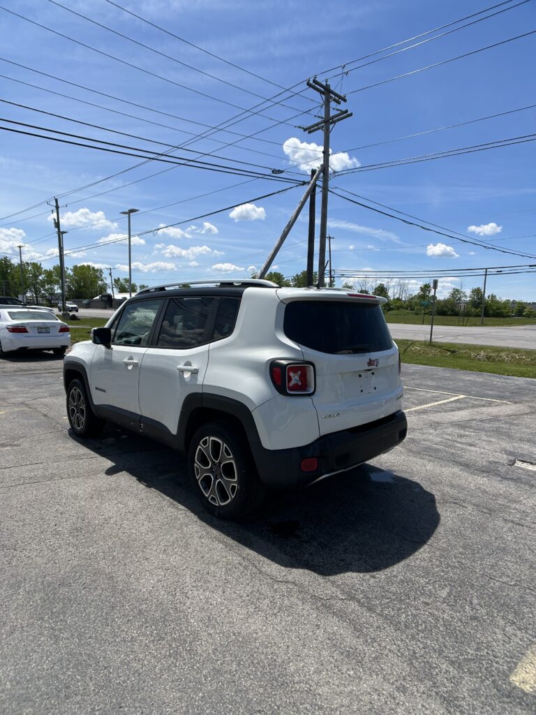 White Jeep SUV parked in a lot with power lines overhead and a bright blue sky in the background.