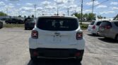 White Jeep Renegade seen from the rear in a parking lot, other vehicles around, blue sky with scattered clouds and overhead power lines.
