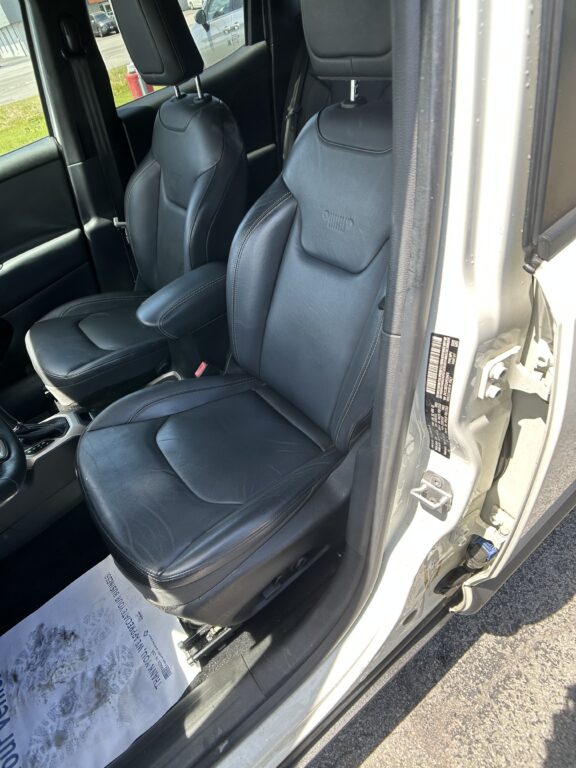 Interior of a car showing black leather front seats with headrests and an open door; outside parking lot visible.