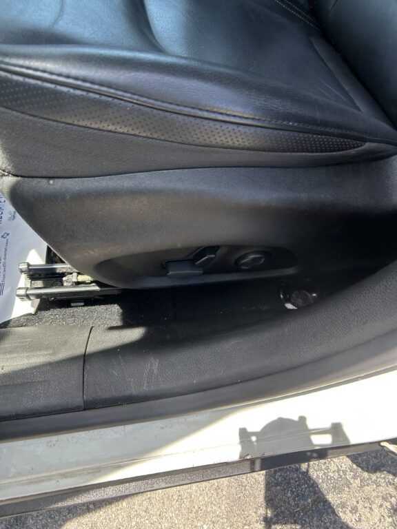 Car seat bottom with visible metal track and adjustment lever underneath leather upholstery.