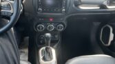 Interior view of a vehicle cockpit: steering wheel on the left, center touchscreen, climate controls, gear shifter, and cup holders between the seats.