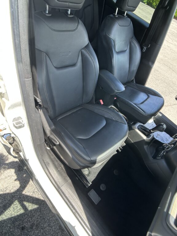 Inside a car showing black leather front seats with white stitching, and the center console with gear shifter visible.