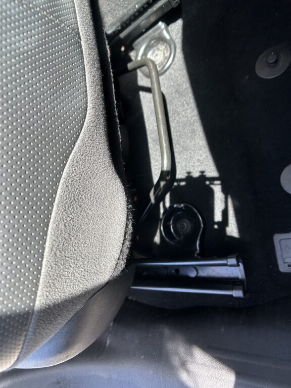 Close-up of the car interior showing a metal seat adjustment lever near the floor by the driver's seat with textured upholstery nearby.