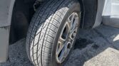 Front right wheel and tire of a light-gray pickup truck, visible fender and wheel well with tread detail and a hint of the vehicle badge on the side.