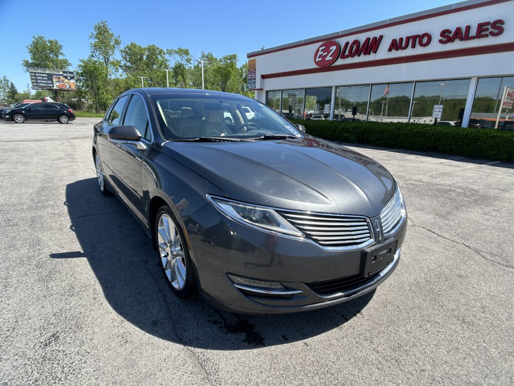 Front-right perspective of a dark gray sedan parked in a car lot in front of an EZ Loan Auto Sales dealership building with a large red sign.