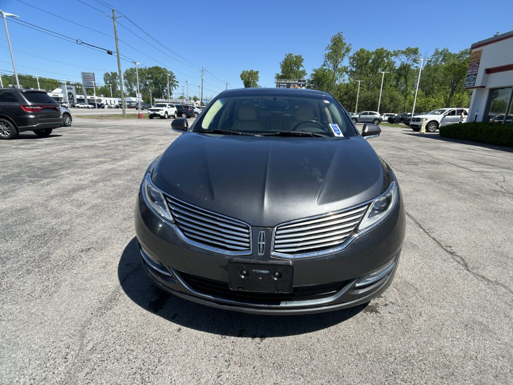 Front view of a dark gray Honda sedan in a car dealership lot on a sunny day, with other vehicles and buildings in the background.