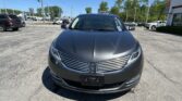 Front view of a dark gray Honda sedan in a car dealership lot on a sunny day, with other vehicles and buildings in the background.