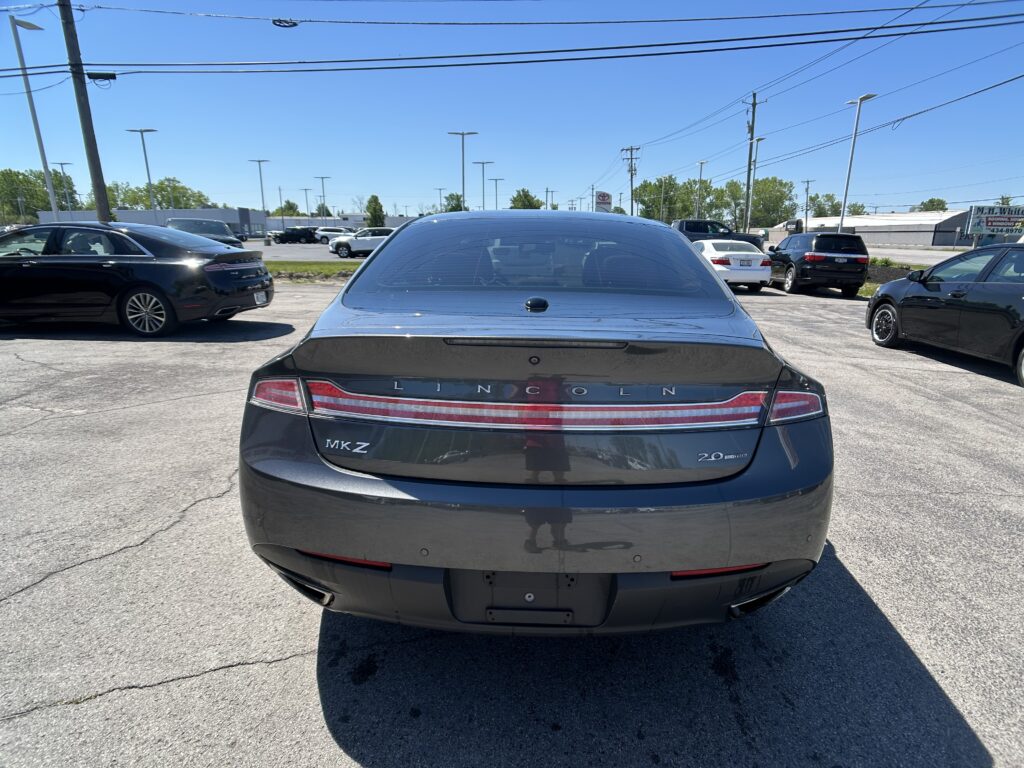 Rear view of a dark gray Lincoln MKZ in a sunny parking lot, with several cars and a Toyota sign in the distance.