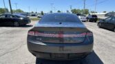 Rear view of a dark gray Lincoln MKZ in a sunny parking lot, with several cars and a Toyota sign in the distance.