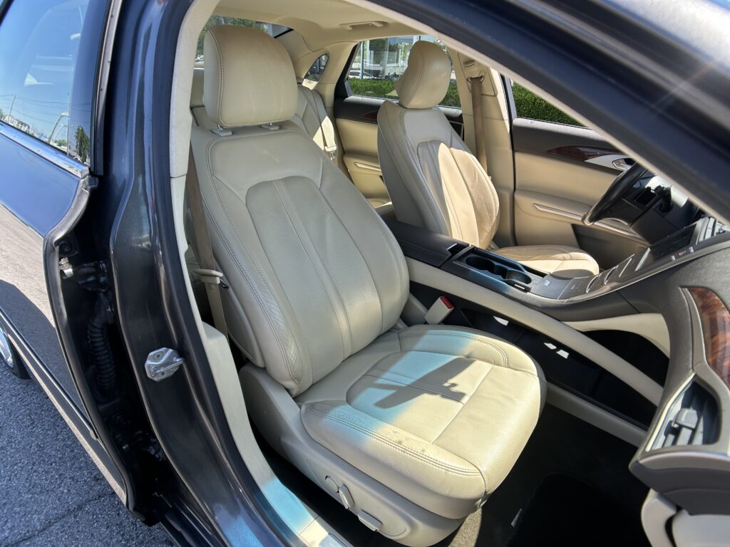 Interior of a beige leather car with front seats visible, passenger door open and cupholders in center console