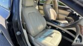 Interior of a beige leather car with front seats visible, passenger door open and cupholders in center console