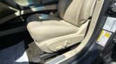 Beige car interior focusing on the front passenger seat with center console and door frame visible, sunlight highlighting the leather upholstery and seat belt buckle nearby.