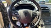 Driver's view of a car interior focusing on the steering wheel and dashboard, with the driver's door open and a dealership lot visible outside through the windshield