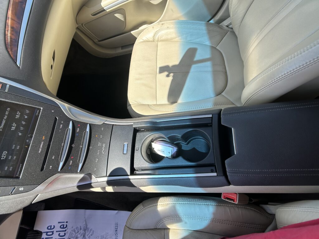 Interior of a car with beige leather seats, center console, and cup holders visible; sunlight casts a shadow across the seat area.