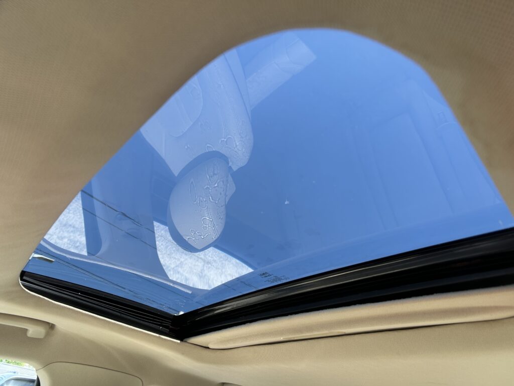 View through an open car sunroof showing blue sky, beige car interior framing the glass.