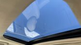 View through an open car sunroof showing blue sky, beige car interior framing the glass.