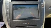 Car infotainment screen showing rearview camera with colored guide lines (green, yellow, red) over a parking lot view
